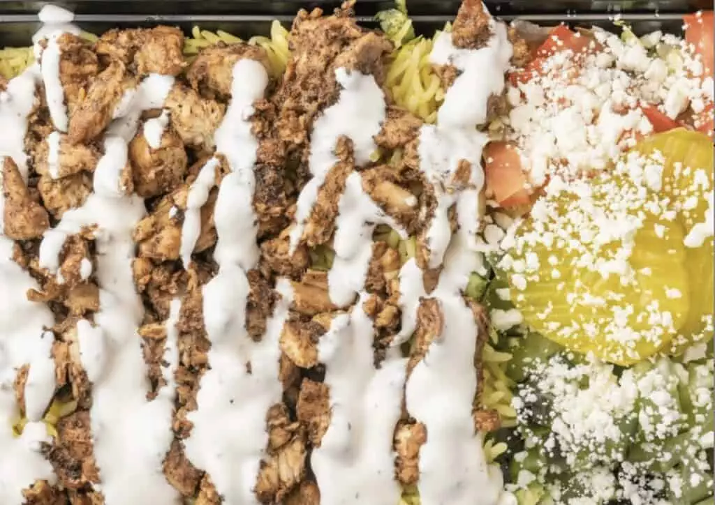 Chicken shawarma platter with rice, salad, pickles, and tzatziki sauce on top.